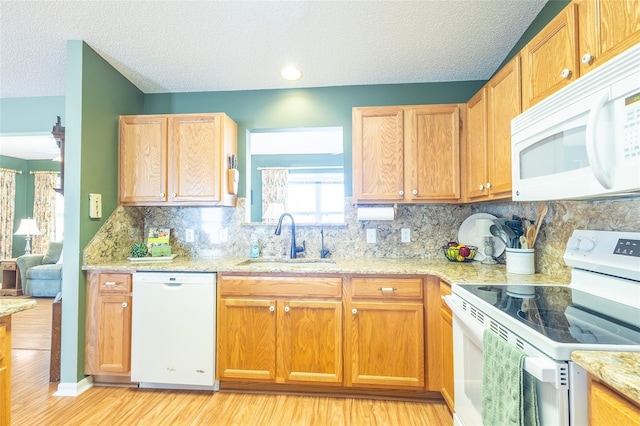 kitchen with light stone counters, white appliances, a sink, light wood-style floors, and decorative backsplash