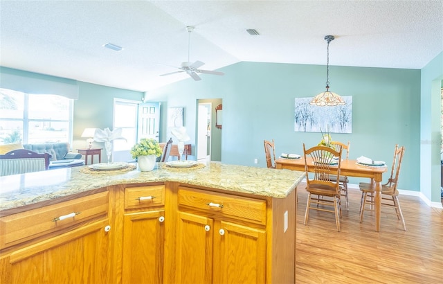 kitchen with brown cabinets, visible vents, light wood-style flooring, open floor plan, and vaulted ceiling