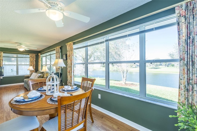 dining space featuring a water view, a textured ceiling, baseboards, and wood finished floors