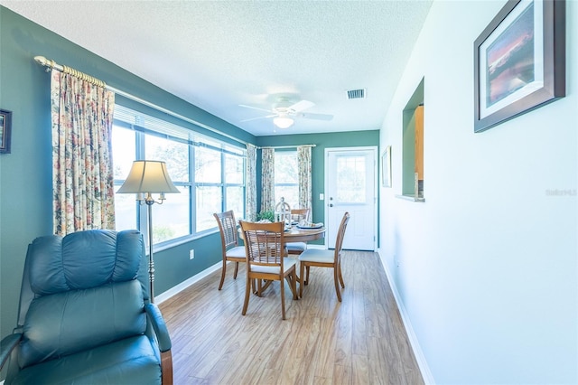 dining space with a textured ceiling, light wood-style flooring, visible vents, and baseboards