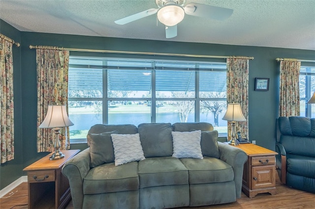 living room featuring a ceiling fan, a textured ceiling, baseboards, and wood finished floors