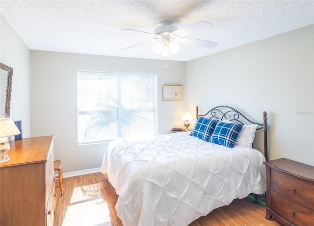 bedroom featuring light wood-style floors, a textured ceiling, baseboards, and a ceiling fan