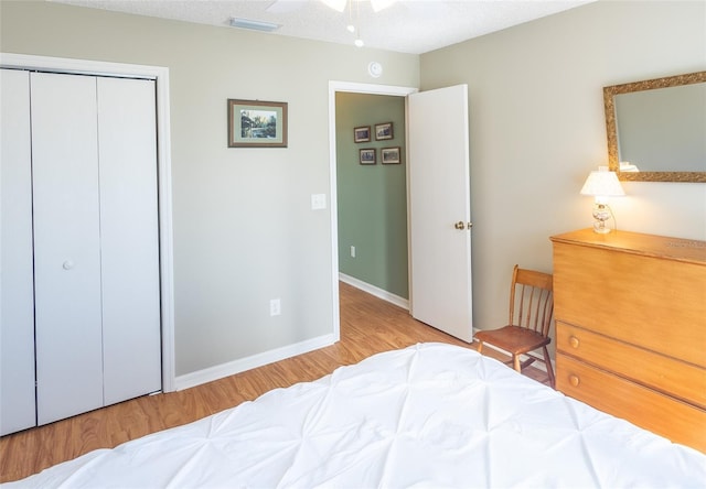 bedroom featuring a textured ceiling, visible vents, baseboards, light wood-style floors, and a closet