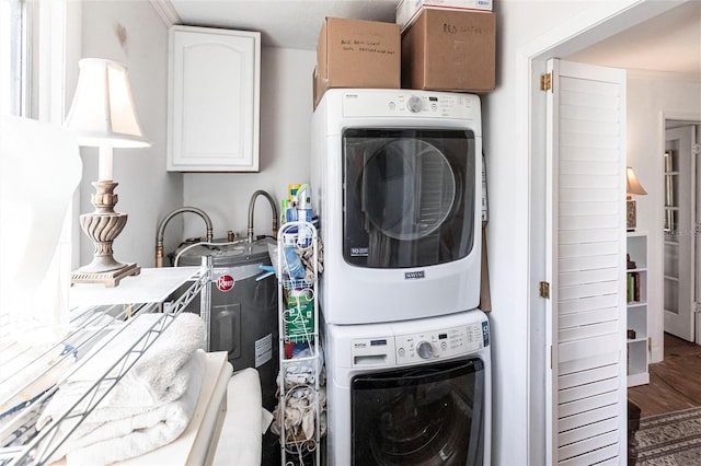 clothes washing area with cabinets, hardwood / wood-style floors, and stacked washer and dryer