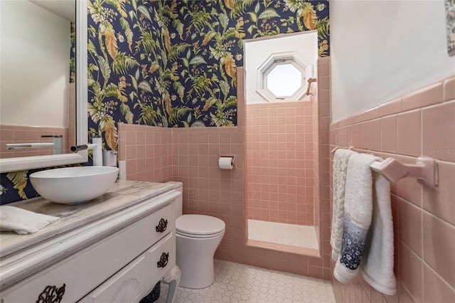 bathroom with tile walls, tiled shower, vanity, tile patterned floors, and toilet