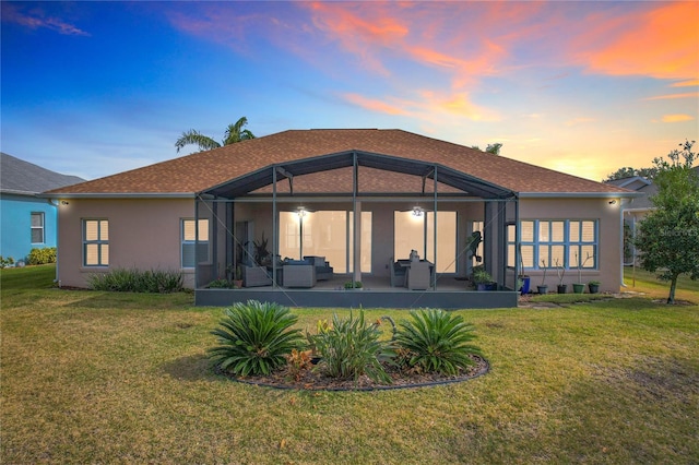 back house at dusk with a patio area, glass enclosure, and a lawn