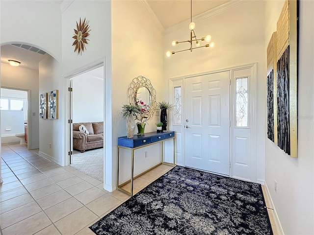 foyer with a high ceiling, crown molding, light tile patterned flooring, and an inviting chandelier