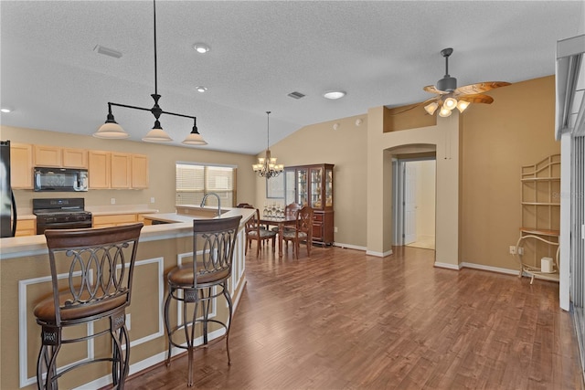 kitchen with a breakfast bar area, dark hardwood / wood-style floors, light brown cabinets, and black appliances