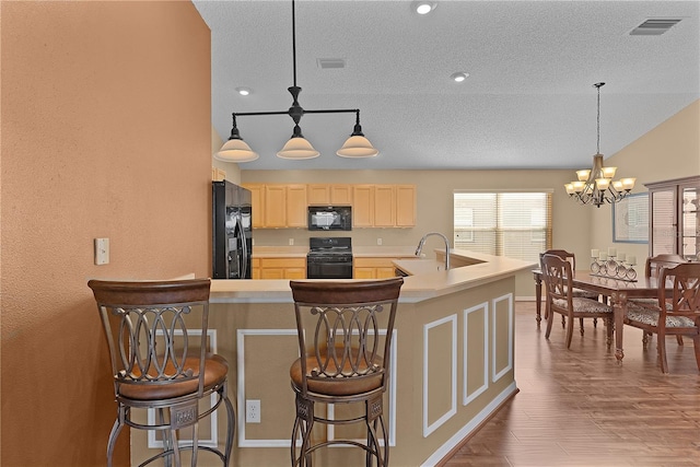 kitchen with wood-type flooring, a breakfast bar, light brown cabinets, and black appliances