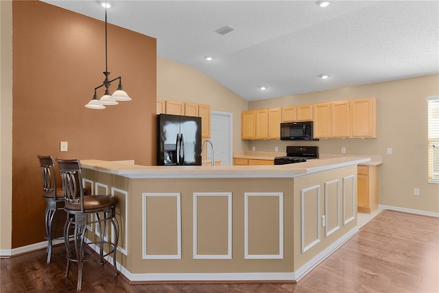 kitchen with pendant lighting, black appliances, lofted ceiling, a breakfast bar area, and kitchen peninsula