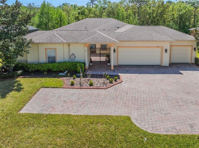 ranch-style house with stucco siding, a front lawn, a gate, decorative driveway, and an attached garage