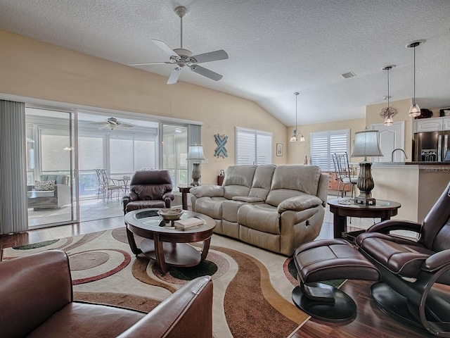 living room with ceiling fan, lofted ceiling, a textured ceiling, and light wood-type flooring