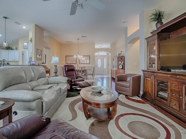 living room featuring ceiling fan with notable chandelier, light hardwood / wood-style flooring, and a textured ceiling