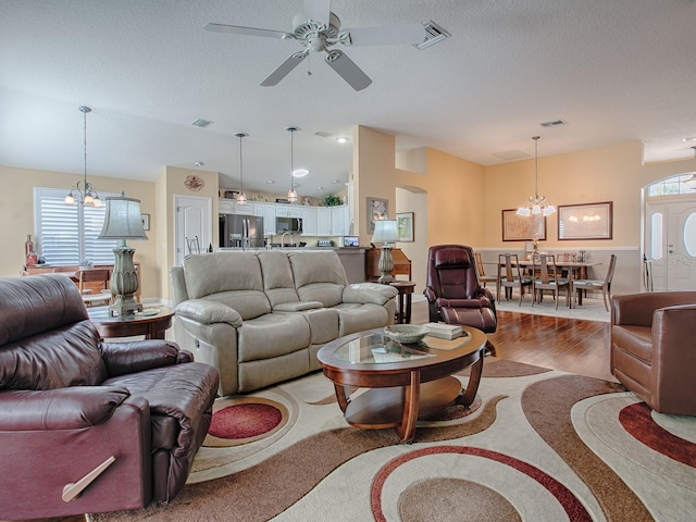 living room featuring lofted ceiling, ceiling fan with notable chandelier, a textured ceiling, and hardwood / wood-style flooring