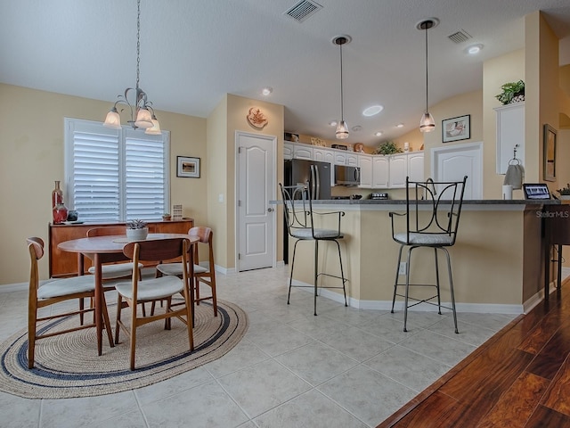 kitchen featuring vaulted ceiling, decorative light fixtures, white cabinets, a kitchen bar, and black fridge with ice dispenser