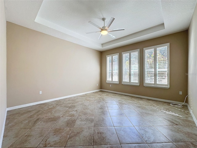 tiled spare room featuring a tray ceiling, a textured ceiling, and ceiling fan