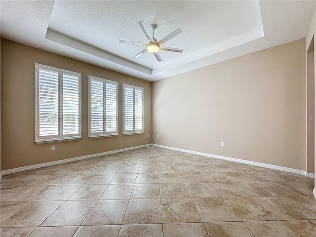 empty room with light tile patterned flooring, ceiling fan, a tray ceiling, and a textured ceiling