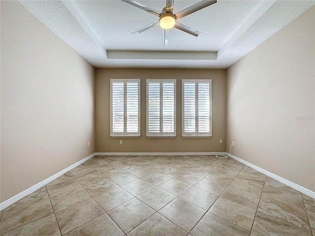 tiled empty room featuring a raised ceiling, ceiling fan, and a textured ceiling