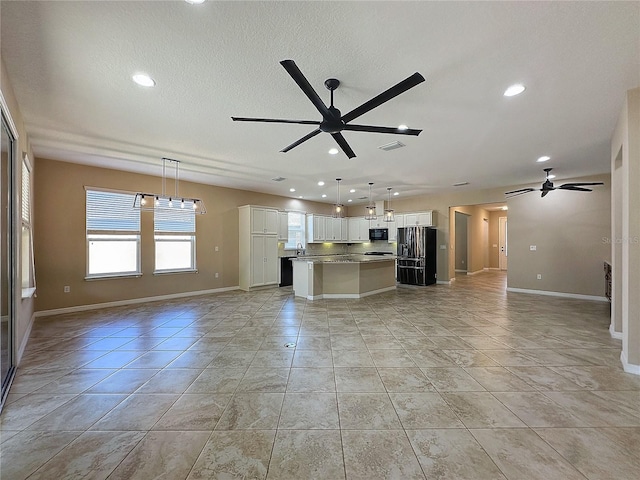 unfurnished living room with light tile patterned floors, white cabinetry, a kitchen island, ceiling fan, and hanging light fixtures