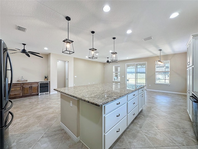 kitchen with black refrigerator, pendant lighting, beverage cooler, a kitchen island, and white cabinetry