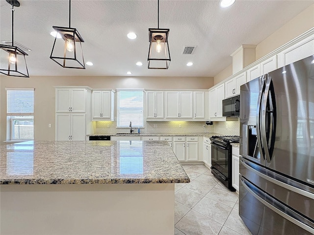 kitchen with hanging light fixtures, light stone countertops, black appliances, sink, and white cabinetry