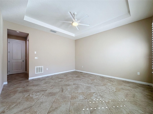 empty room with ceiling fan, light tile patterned floors, a tray ceiling, and a textured ceiling