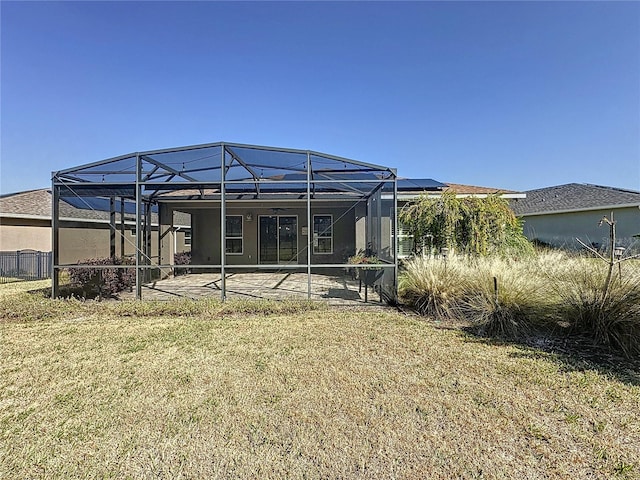 back of property featuring glass enclosure, a lawn, and a patio area