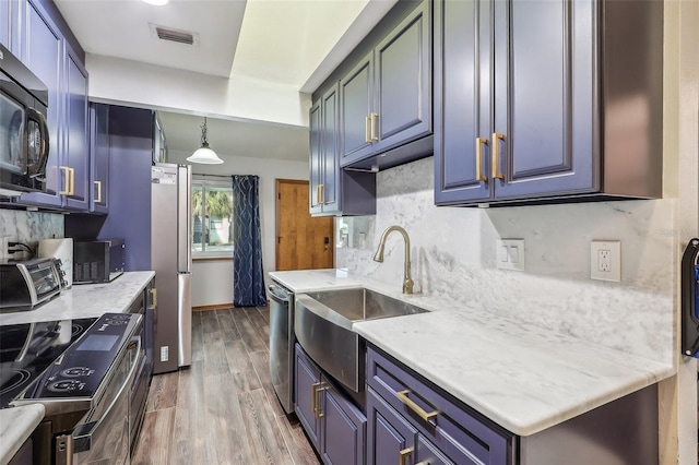 kitchen with sink, wood-type flooring, hanging light fixtures, appliances with stainless steel finishes, and decorative backsplash