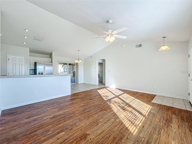 unfurnished living room featuring ceiling fan with notable chandelier, lofted ceiling, light hardwood / wood-style floors, and a textured ceiling