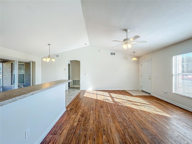 unfurnished living room featuring lofted ceiling, ceiling fan with notable chandelier, a textured ceiling, and light hardwood / wood-style flooring