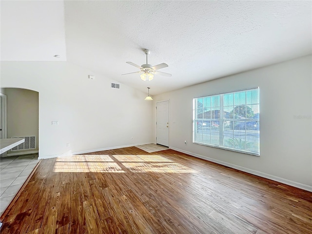 unfurnished living room featuring ceiling fan, lofted ceiling, a textured ceiling, and light hardwood / wood-style flooring