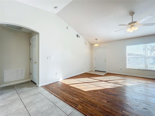 spare room featuring ceiling fan, lofted ceiling, a textured ceiling, and light wood-type flooring