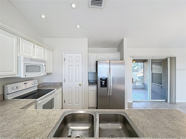 kitchen with sink, white appliances, light tile patterned floors, a textured ceiling, and white cabinets