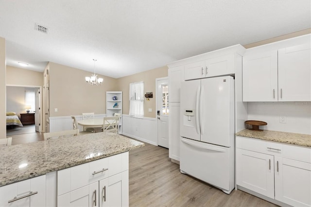 kitchen with light stone counters, hanging light fixtures, light wood-type flooring, white fridge with ice dispenser, and white cabinets