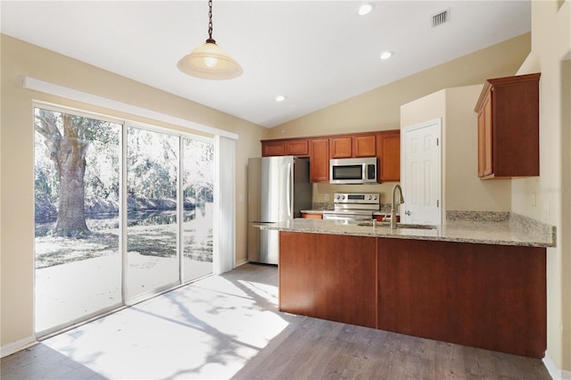 kitchen featuring vaulted ceiling, appliances with stainless steel finishes, pendant lighting, sink, and light stone countertops