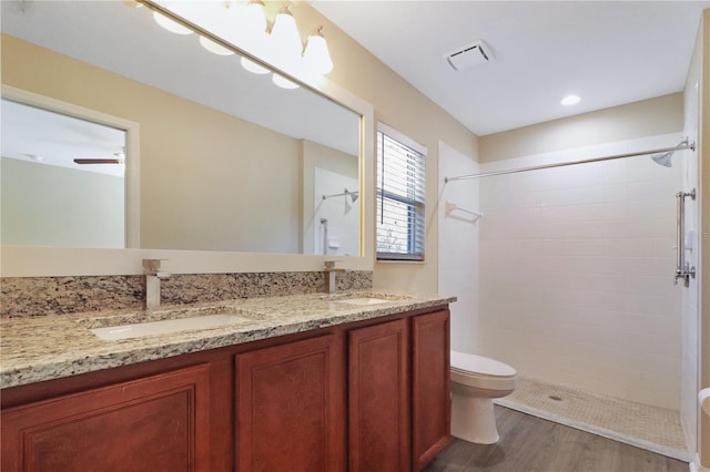 bathroom featuring vanity, wood-type flooring, tiled shower, and toilet