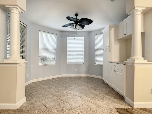 unfurnished dining area with decorative columns, a healthy amount of sunlight, light tile patterned floors, and ceiling fan