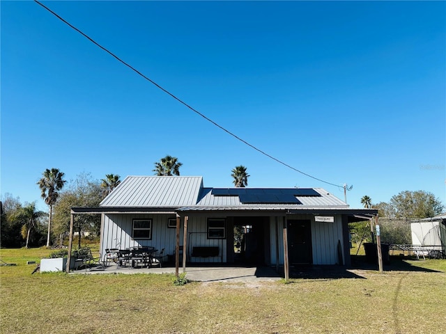 rear view of property featuring a patio, a yard, and solar panels