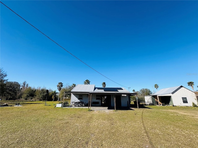 rear view of property featuring a lawn and solar panels