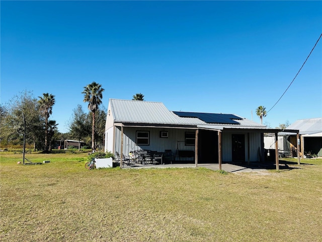 rear view of property featuring a patio, a yard, and solar panels