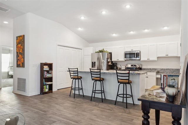 kitchen featuring a breakfast bar area, appliances with stainless steel finishes, white cabinetry, light stone counters, and an island with sink