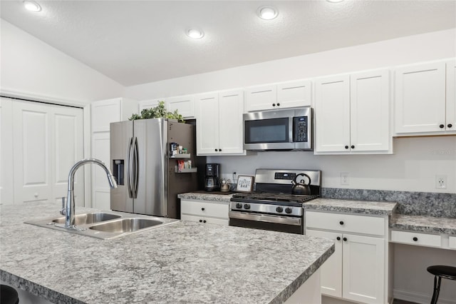 kitchen featuring sink, vaulted ceiling, an island with sink, stainless steel appliances, and white cabinets