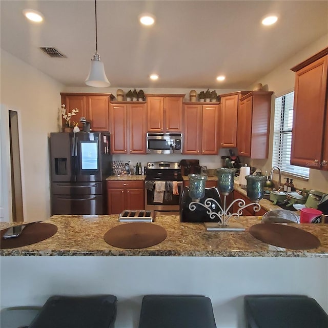 kitchen with light stone countertops, stainless steel appliances, hanging light fixtures, and a kitchen bar