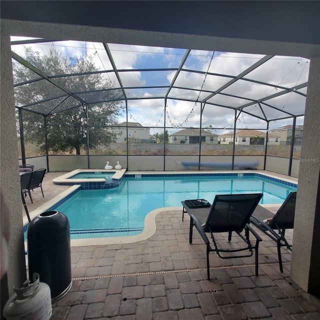 view of pool with a patio, glass enclosure, and an in ground hot tub