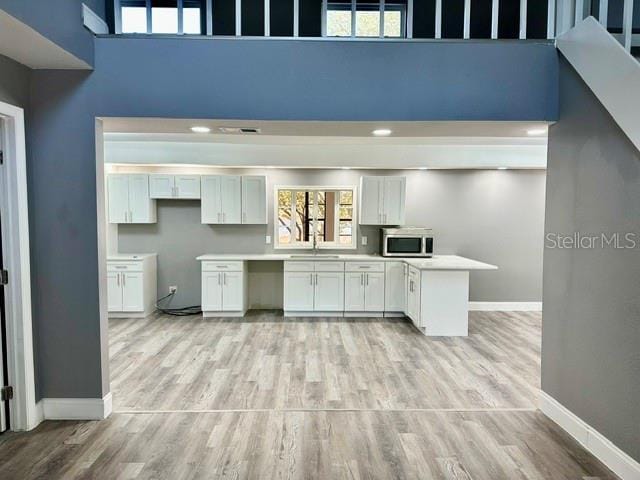 kitchen with white cabinetry, light hardwood / wood-style floors, sink, and a high ceiling