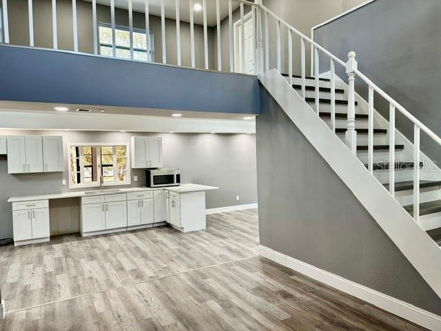 interior space featuring white cabinetry, sink, light hardwood / wood-style floors, and a high ceiling