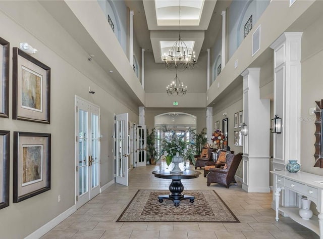 tiled foyer entrance with ornate columns, an inviting chandelier, and french doors