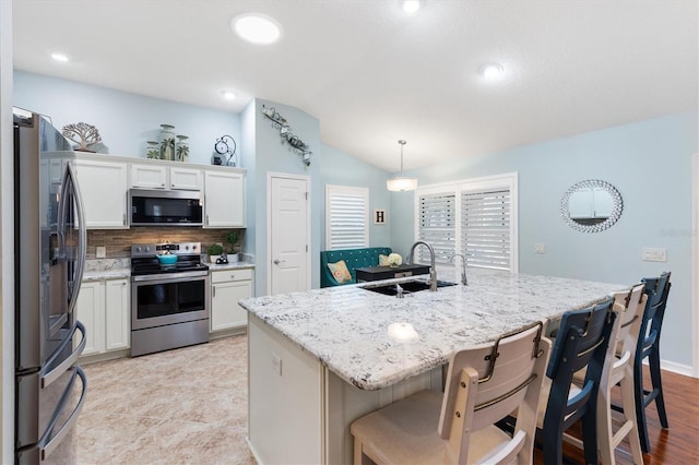 kitchen featuring pendant lighting, lofted ceiling, appliances with stainless steel finishes, white cabinetry, and a center island with sink