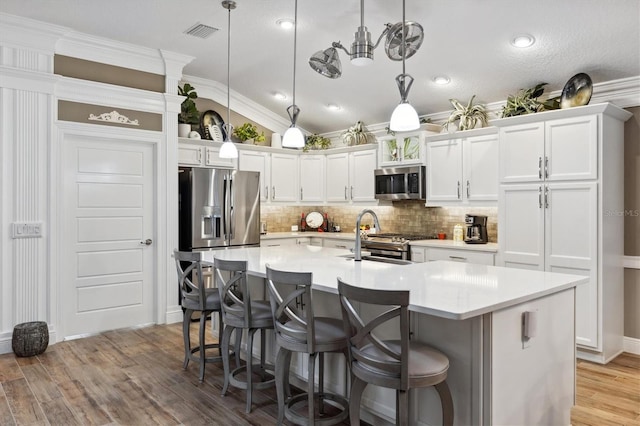 4515 Biggs Pl, The Villages, FL 32163 - kitchen featuring white cabinets, appliances with stainless steel finishes, tasteful backsplash, a breakfast bar area, and light wood-type flooring