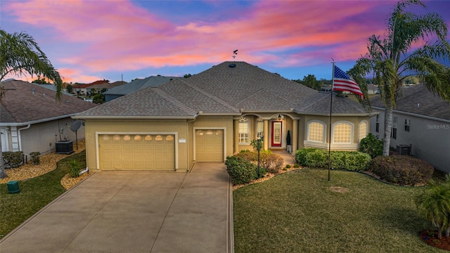 french country home with concrete driveway, a lawn, an attached garage, central AC, and stucco siding